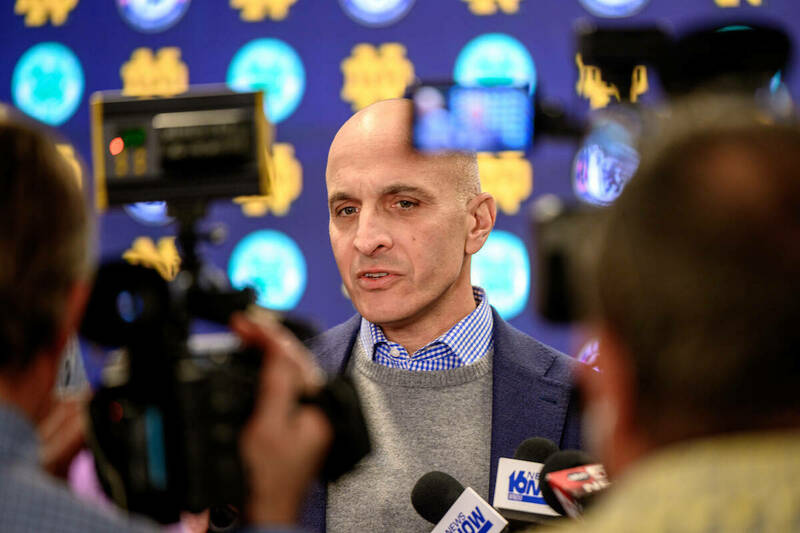 Incoming athletic director Pete Bevacqua, surrounded by cameras and microphones, stands in front of a backdrop with interlocking ND logos.
