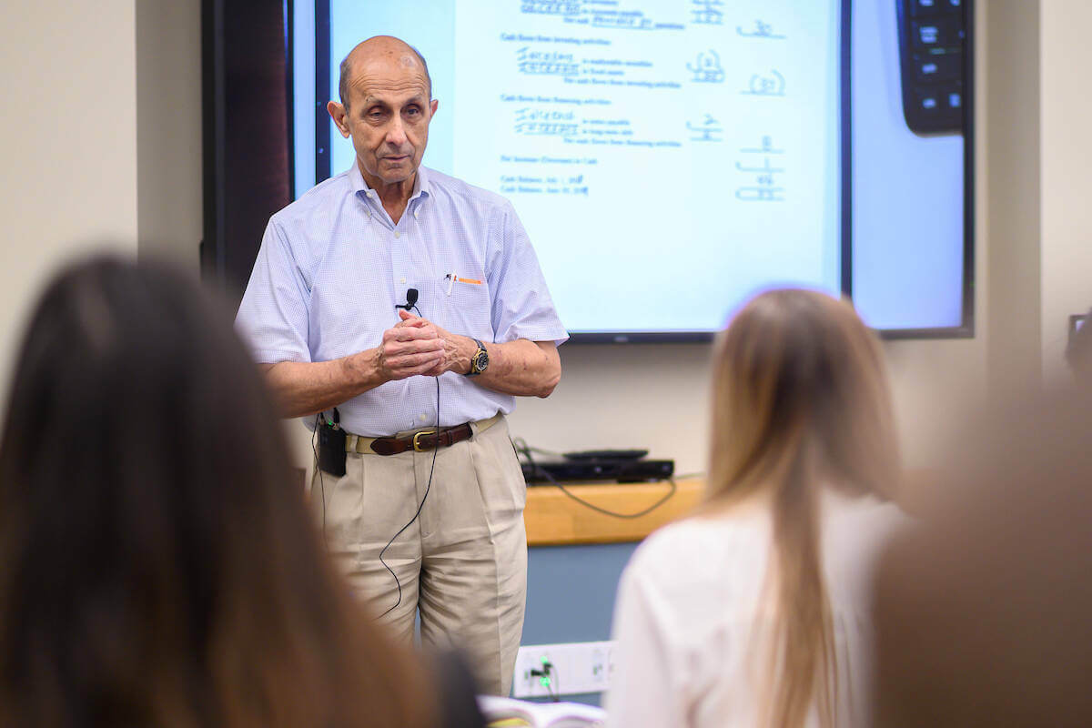 Accounting professor Ken Milani stands in front of a screen projecting data as he talks to students in the classroom.