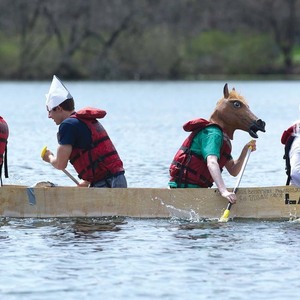 Students in unusual headgear, including a Cookie Monster hat and a horse head, row their boat in the Fisher Regatta.