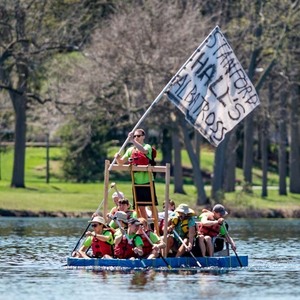 Students on a raft competing in the Fisher Regatta on St. Mary's Lake wave a flag that says 