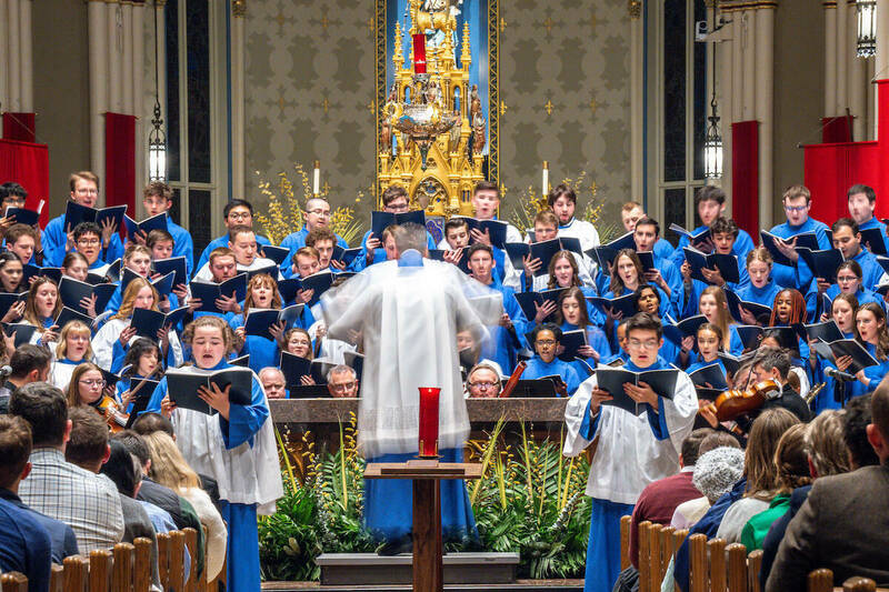 The Notre Dame Liturgical Choir, surrounding conductor Andrew McShane, performs for people in the pews at the Basilica of the Sacred Heart.