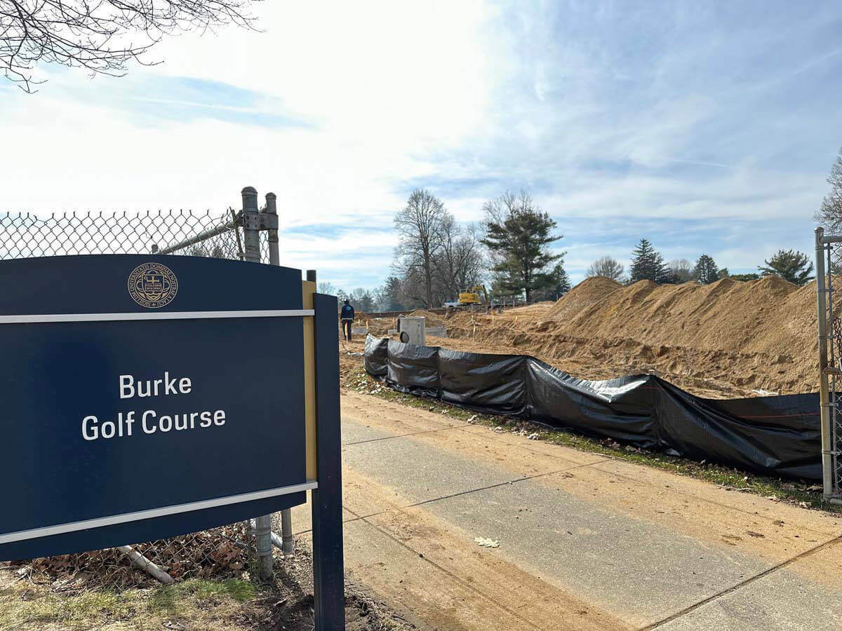 The sign of the Burke Golf Course with dirt mounds in the background as part of the construction project for two new residence halls.