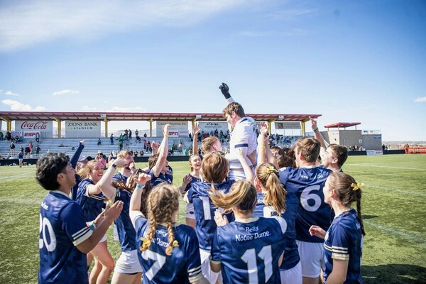A player in a white jersey is hoisted into the air by players in blue in celebration of Notre Dame's Gaelic football national championship