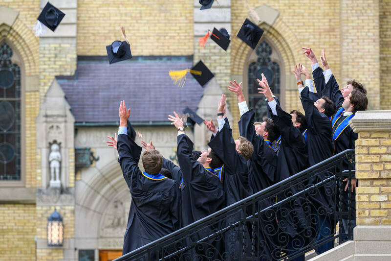 Seniors in caps and gowns toss their caps into the air for a photo celebration their upcoming graduation.