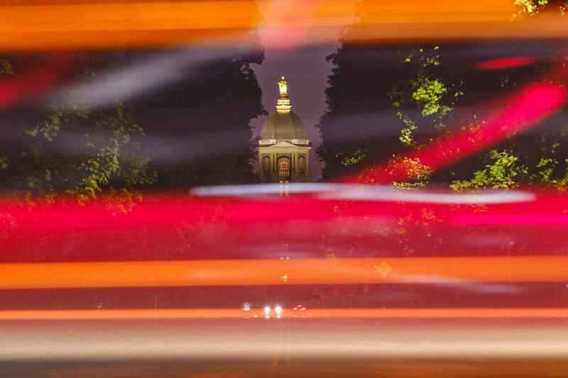 A photo looking north on Notre Dame Avenue to the Golden Dome, surrounded by streaks of red and orange light from the passing cars on Angela Boulevard.