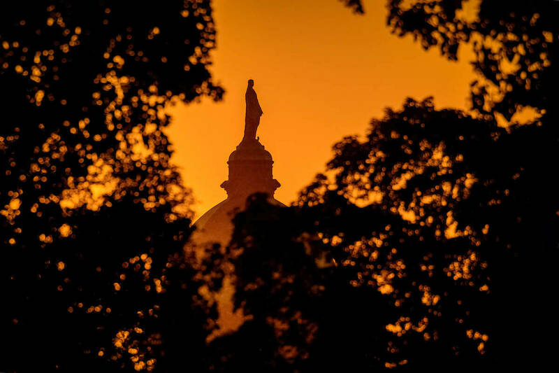An orange sky at sunrise with a silhouette of the Golden Dome and the statue of Mary visitble through a canopy of trees.