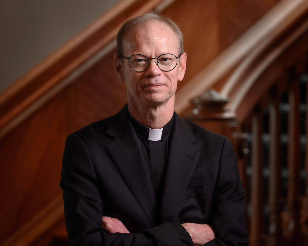 Father Bob Dowd poses for a portrait in his collar with arms folded.