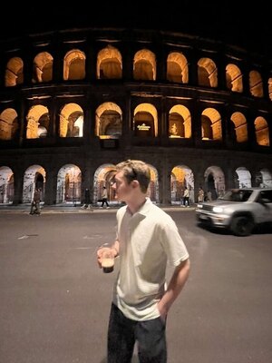 Sam Coffman standing in front of the Roman Colosseum in the evening holding a drink