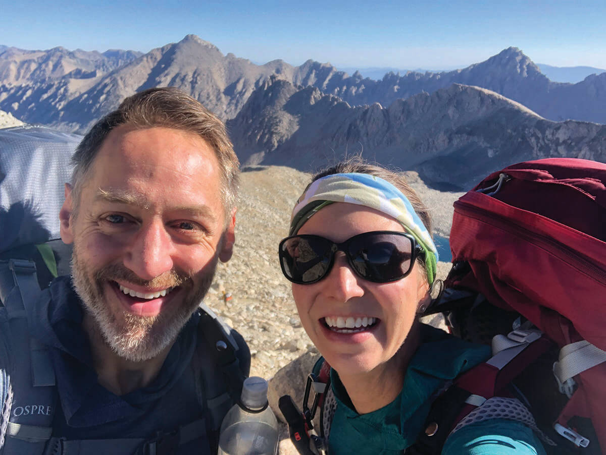 A selfie of Chris and Karen Chiappinelli with mountain peaks in the background along the John Muir Trail