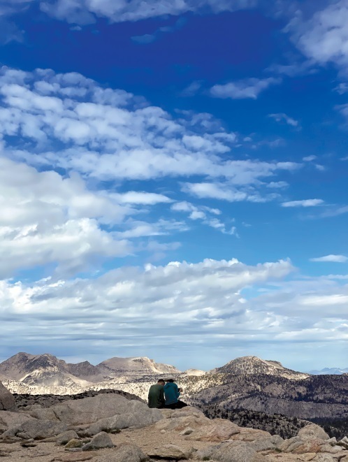 Chris and Karen Chiappinelli photographed from a distance as the rest and take in the scenery of blue sky and mountain peaks along the John Muir Trail