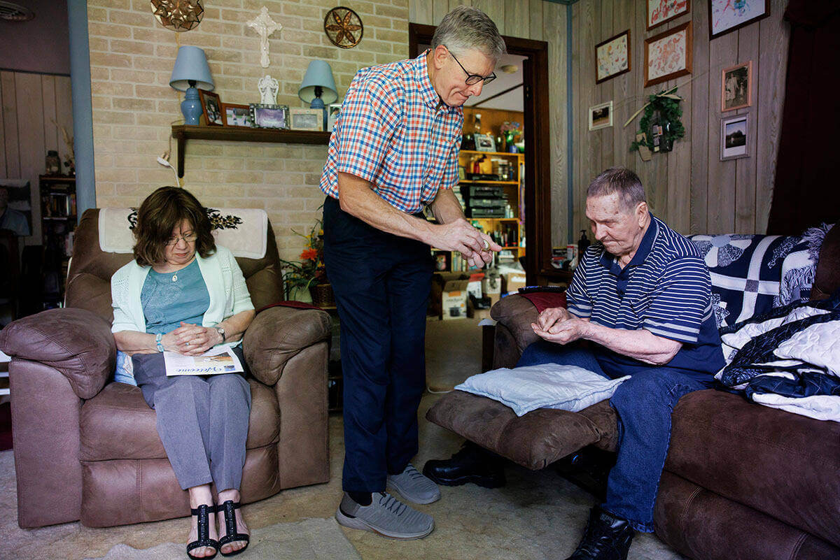 Deacon John Cord stands between two people as he ministers to them during a home visit.