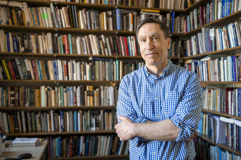 William Cavanaugh poses with his arms folded in his office in front of a large bookshelf