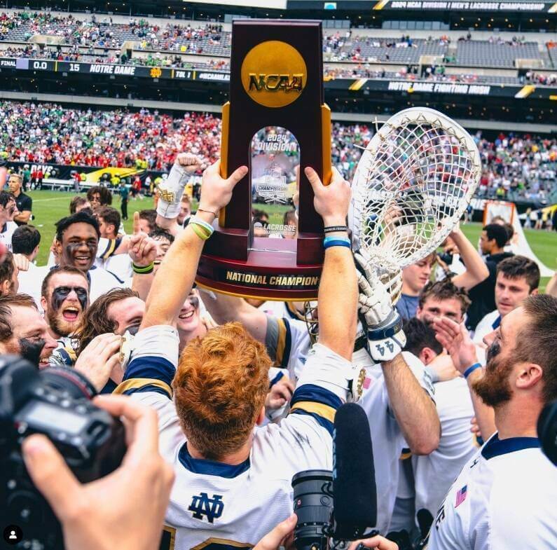 Amid a team celebration, a Notre Dame lacrosse player hoists the 2024 NCAA championship trophy