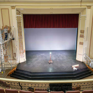 A man on scaffolding to the left of a theater stage.