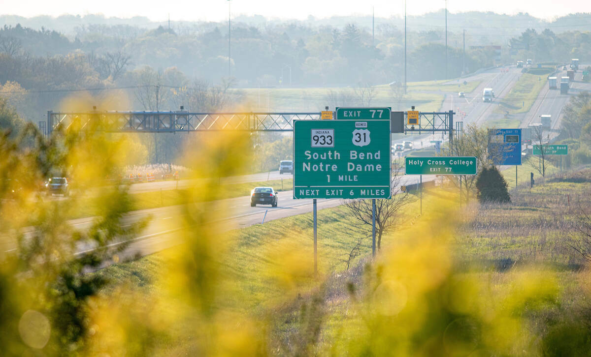 A view through foliage of the South Bend/Notre Dame exit sign on the on the Indiana Toll Road.