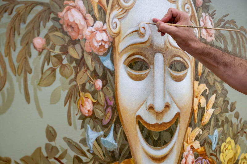 An artist's hand holding a paintbrush puts detailed touches on a six-foot canvas painting of a mask representing comedy to be hung in Washington Hall.