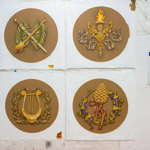 Round painted ceiling medallions representing the Greek god Dionysus, a torch of knowledge, St. Genesius (patron saint of the theater), and a lyre and laurel wreath hang on a studio wall.