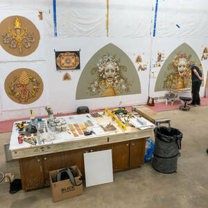 Colorful ornate murals in progress are shown in an art studio.