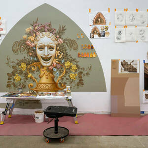 A large ornate mural depicting the laughing face of comedy theater surrounded by flowers hangs on a studio wall.