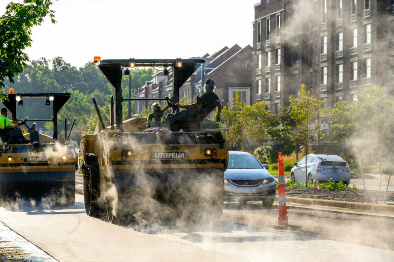 Large asphalt pavers in a cloud of dust during a construction project on Angela Boulevard