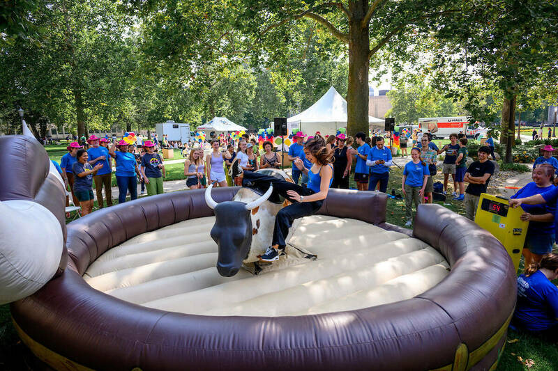 A woman falls off a mechanical bull onto a bouncy cushion.