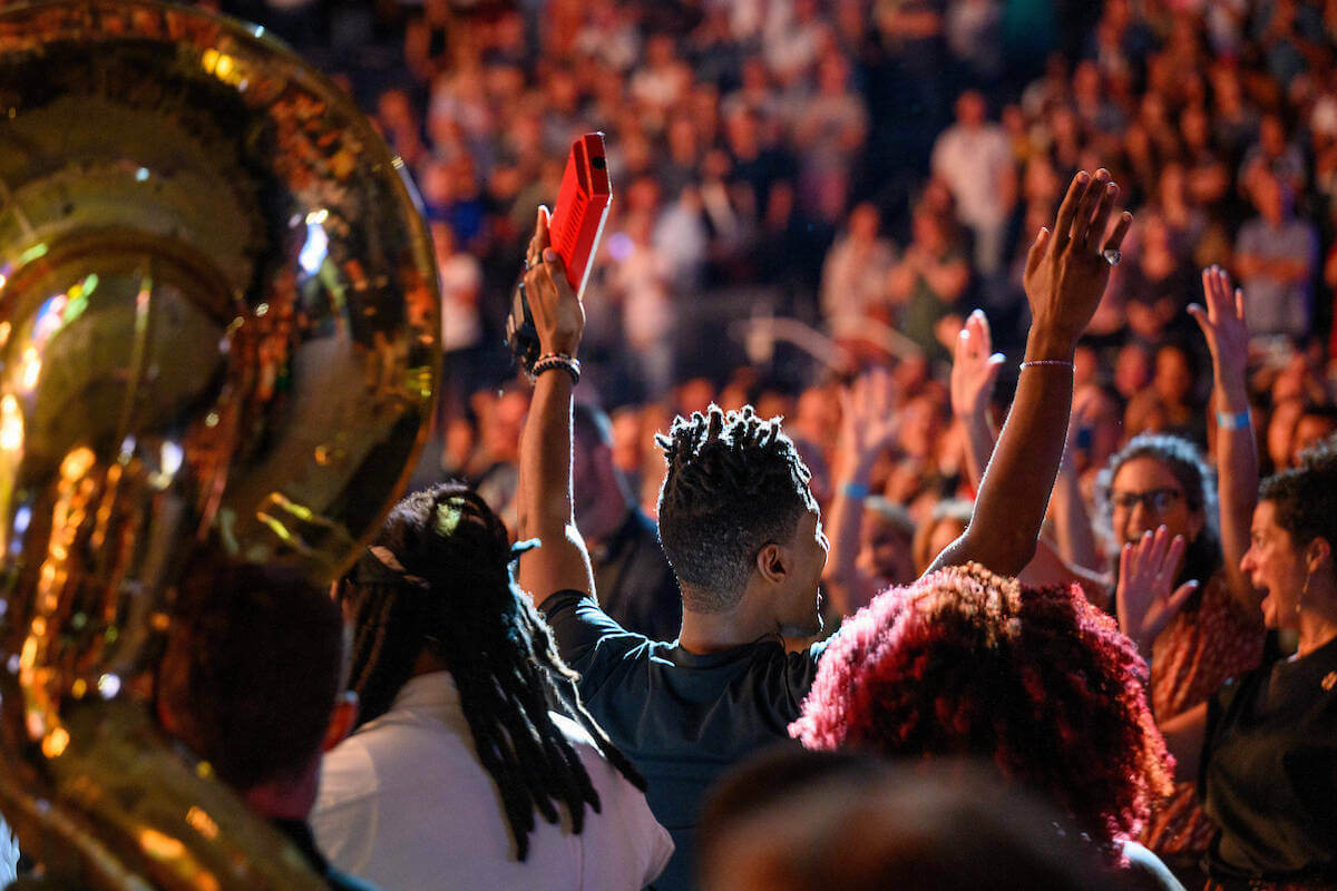 Musician Jon Batiste raises his arms as he leads a student brass band through the crowd during his concert at Purcell Pavilion