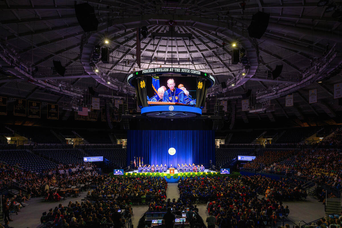 An image of Rev. Robert A. Dowd on a video screen and the crowd in Purcell Pavilion as he delivers his inaugural address