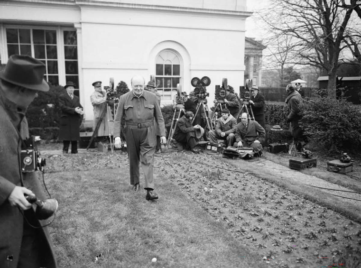 Winston Churchill, wearing his characteristic siren suit,walks on the White House lawn in 1942, surrounded by photojournalists