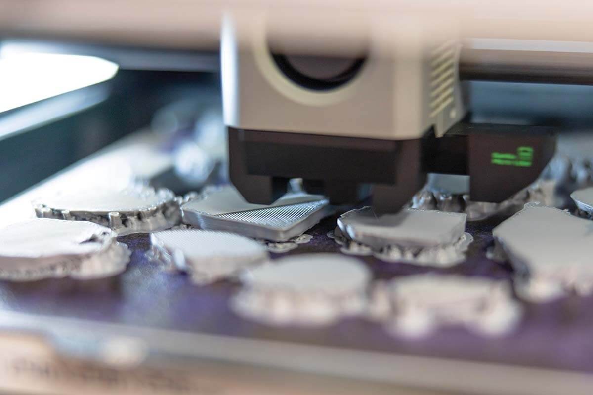 A 3D printer deposits layers of silver material onto a platform covered with partially completed objects.