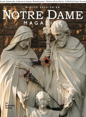White marble statues depict Mary, Joseph, and child Jesus. Mary's hands are crossed, Joseph holds a lily staff. Both look down at the child, who points upwards. Red and orange flowers are draped on them.