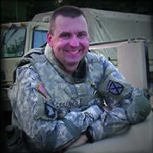 Smiling man in US Army ACU uniform with "DURHAM" nametag and 82nd Airborne Division patch, against military vehicle.
