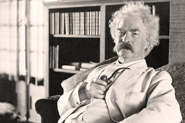 Author Mark Twain, with white hair, a thick moustache and wearing a white suit, leans back in his chair, holding a pipe.